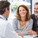 Modern klinikte güler yüzlü doktorla danışan orta yaşlı çift, doğal ışık ve Türk kültürel unsurlarla desteklenen sağlık ortamı