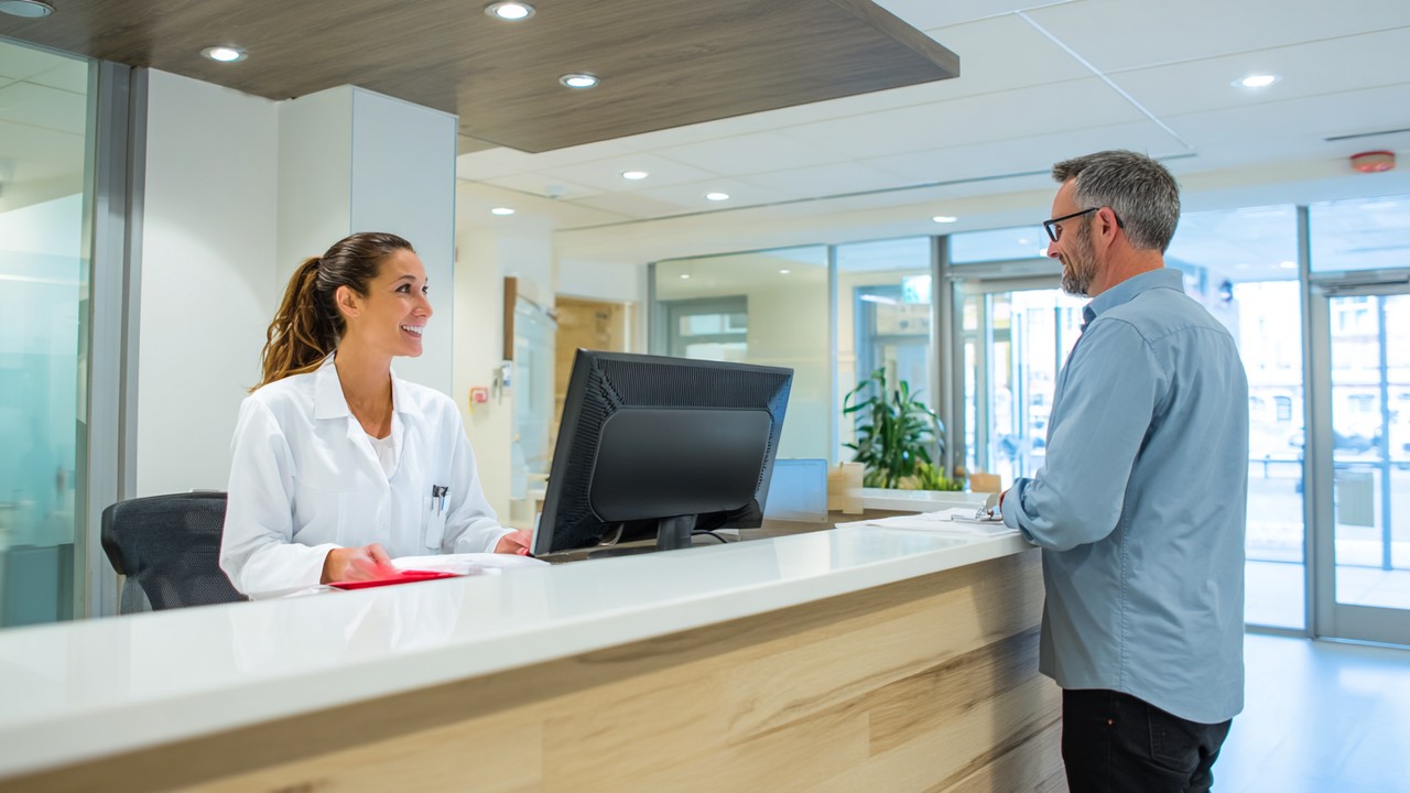 Modern sağlık kliniği resepsiyon alanında güler yüzlü resepsiyonist ve hasta, temiz ve profesyonel ortam, güven verici sağlık hizmeti