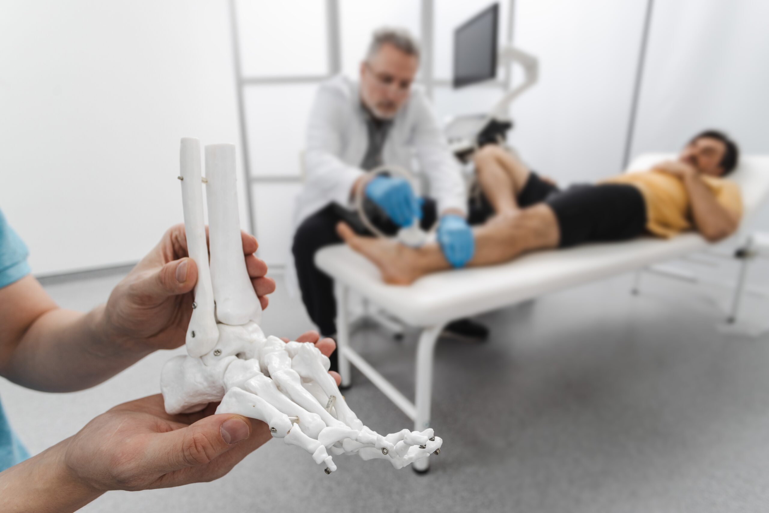 Anatomical model of foot bones against the background of the diagnostic process of a patient's injured leg
