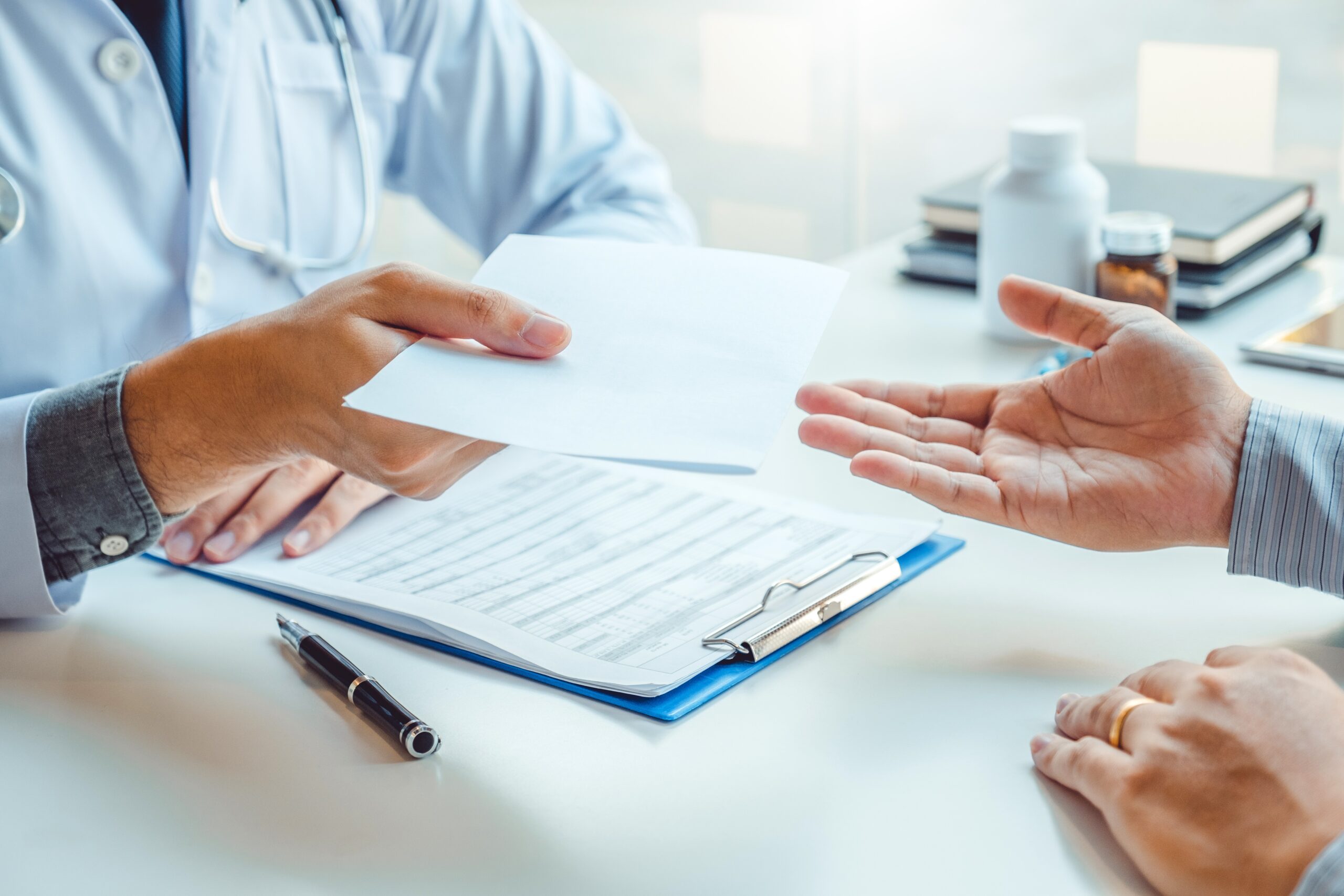 Doctor or physician writing a diagnosis and giving a medical prescription to a male patient