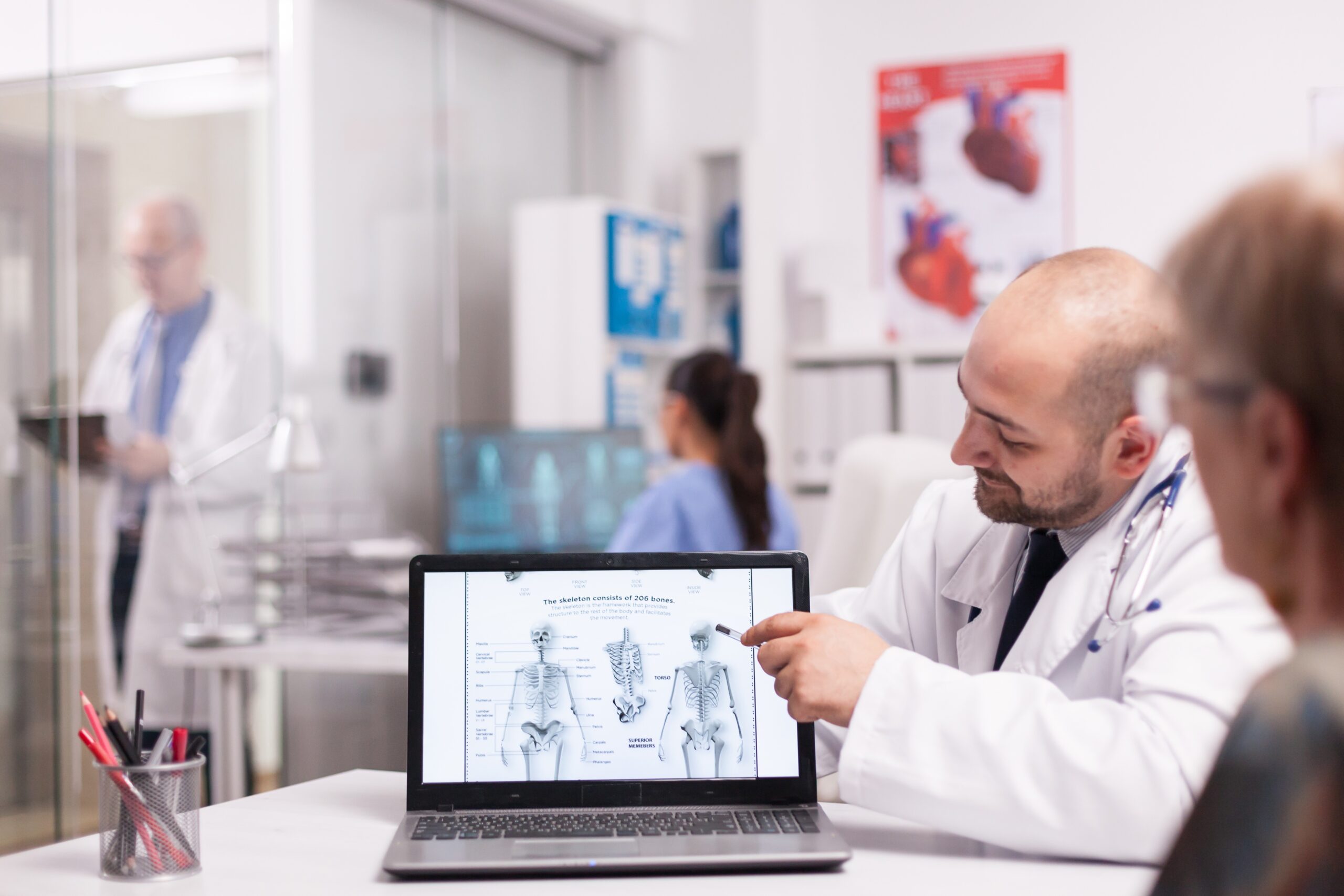 Doctor pointing at human skeleton on laptop