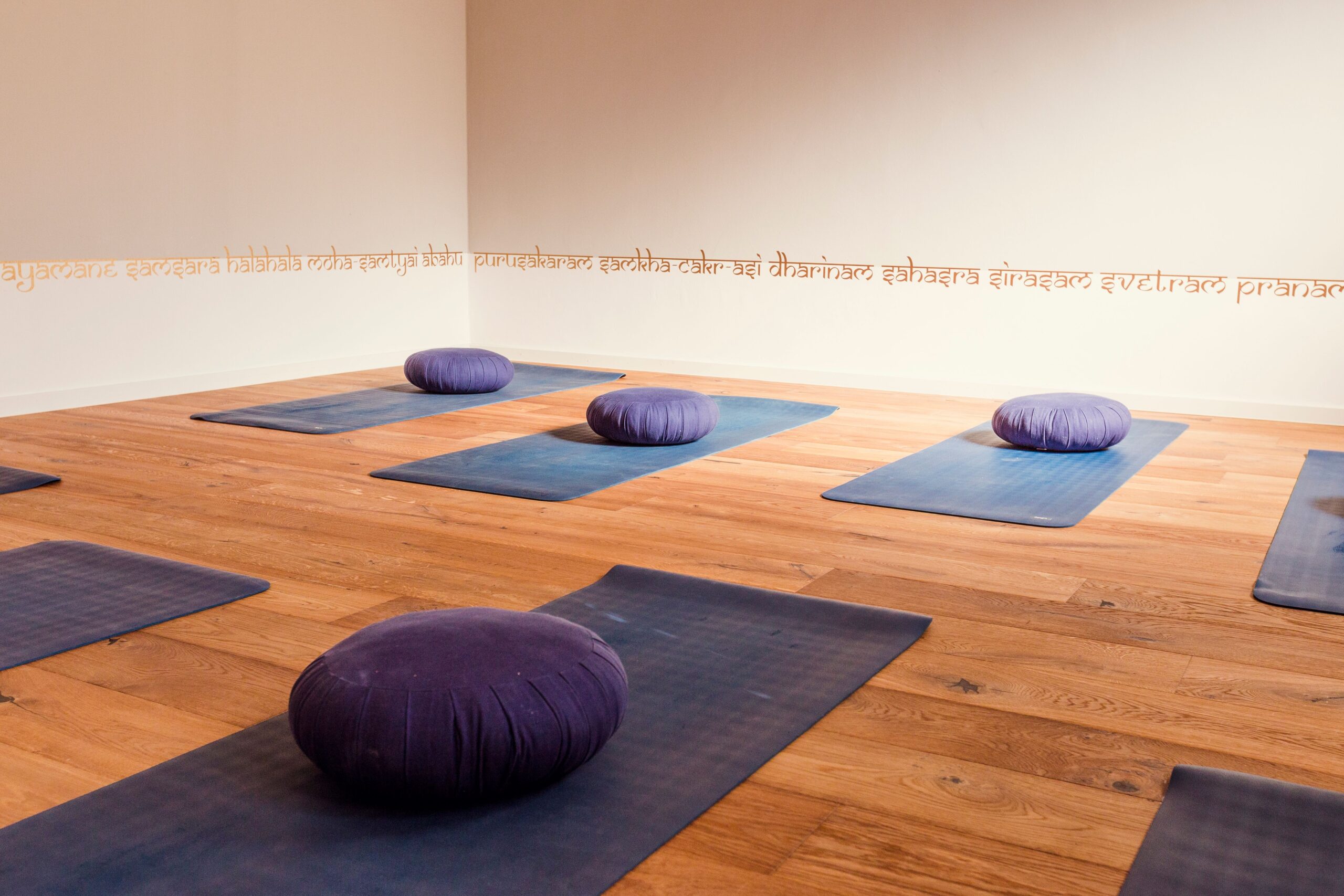 Çeşitli yoga matları, köşede Buddha heykeli ile birlikte ahşap zemin üzerinde