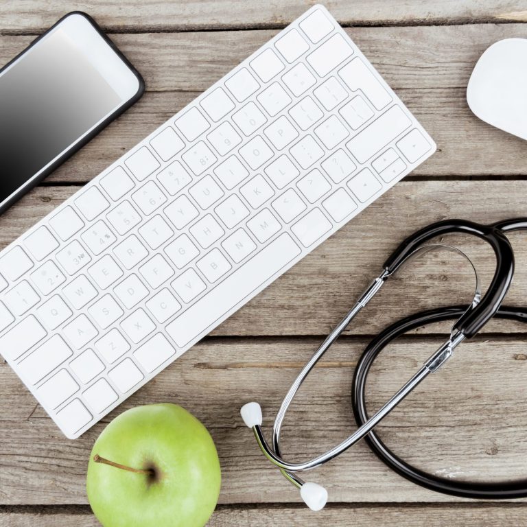 flat lay with digital devices, stethoscope and fresh apple on wooden table