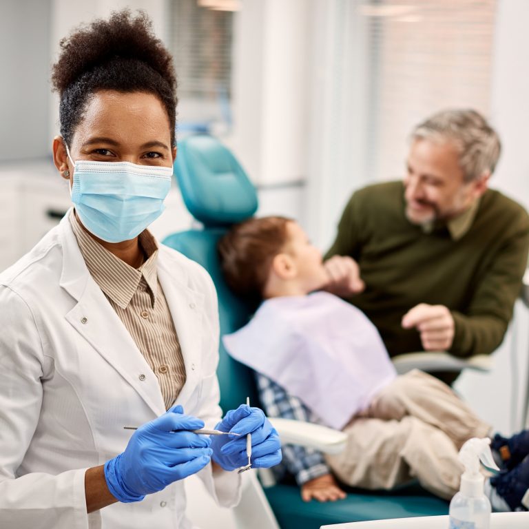 Happy African American stomatologist at dentist's office with her patients in the background.